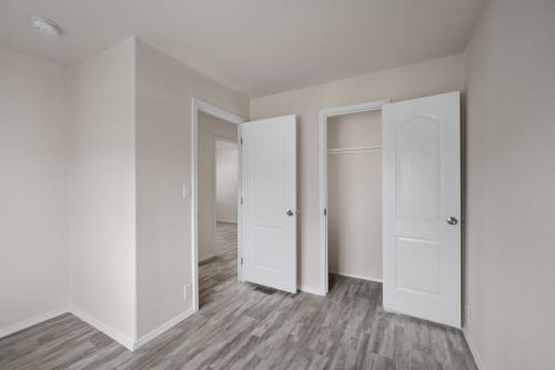 An empty room with white doors and wood floors.